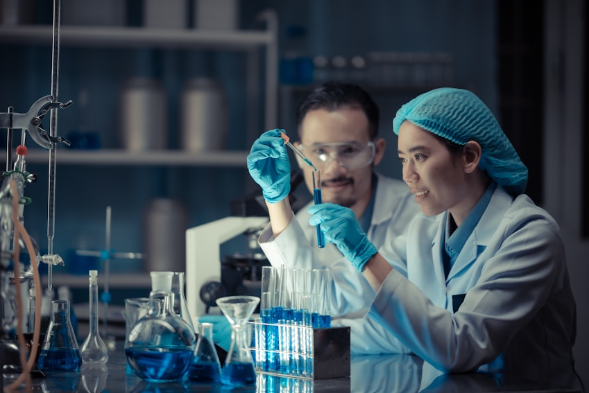 Two scientists in a laboratory using a pipette to drop a sample into a test tube filled with blue liquid.
